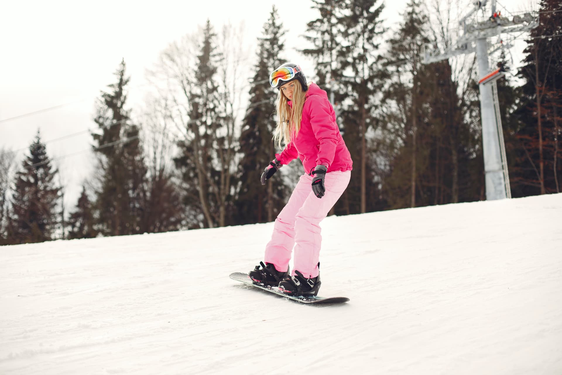 Girl snowboarding under a lift wearing a bright pink ski outfit