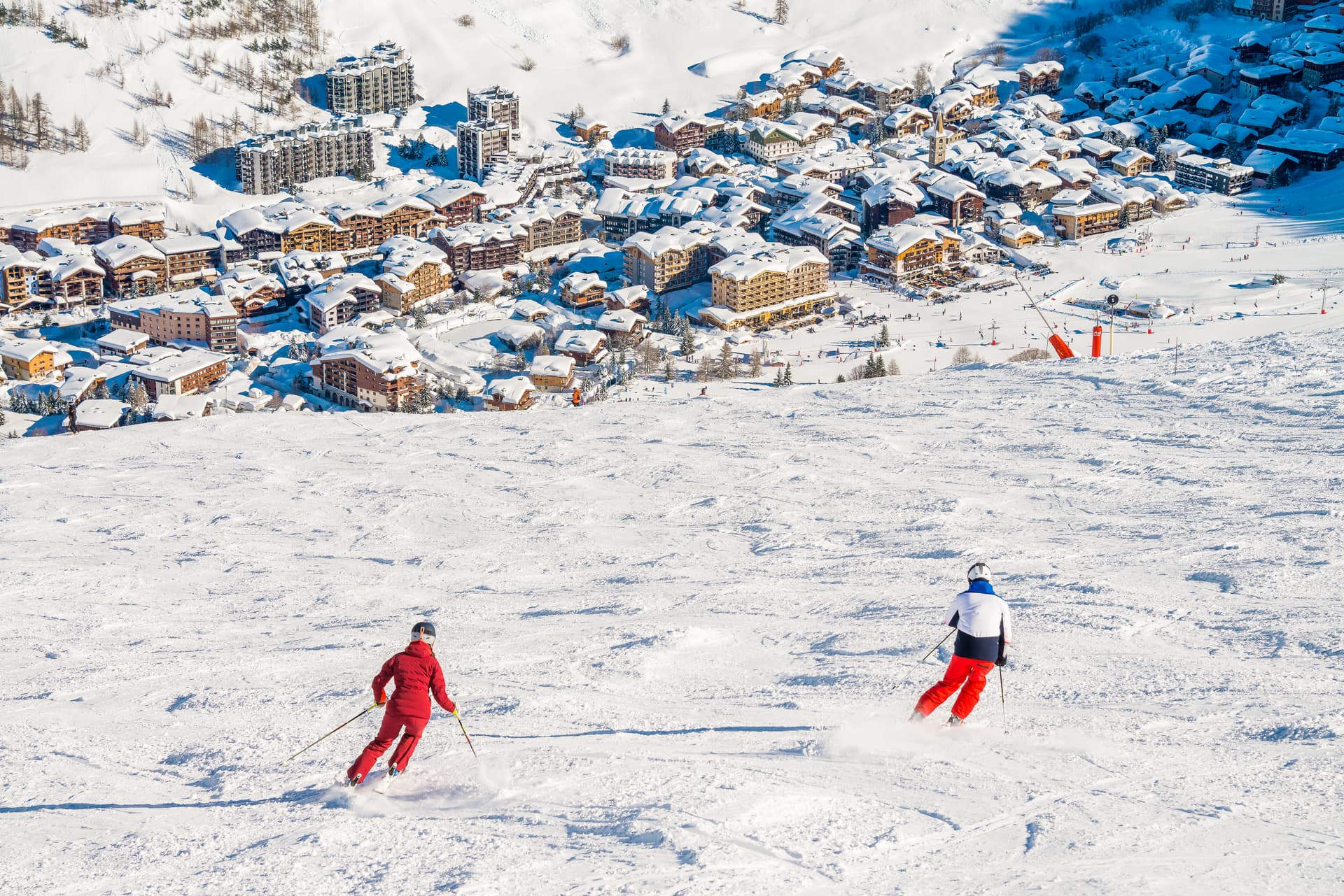 Two skiiers skiing down slope towards Val D'isere town centre in French Alps